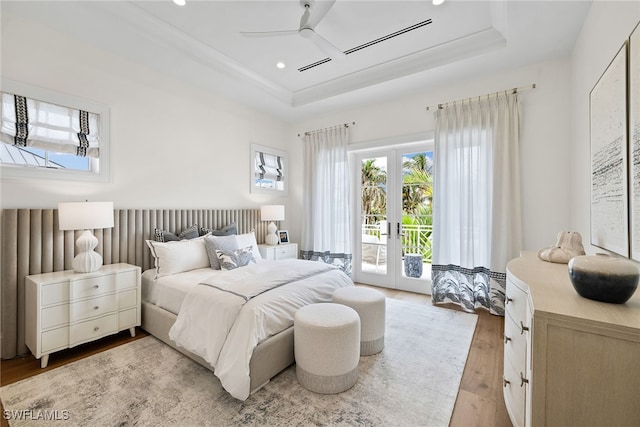 bedroom featuring light hardwood / wood-style floors, a raised ceiling, access to outside, and french doors