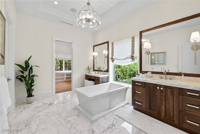 bathroom featuring a notable chandelier, a raised ceiling, a washtub, and vanity