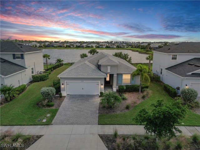 view of front of home with a garage, a water view, and a lawn