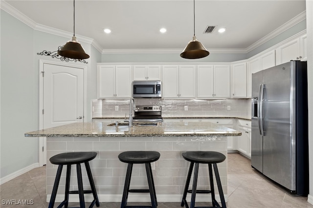 kitchen with light stone counters, white cabinets, stainless steel appliances, and an island with sink