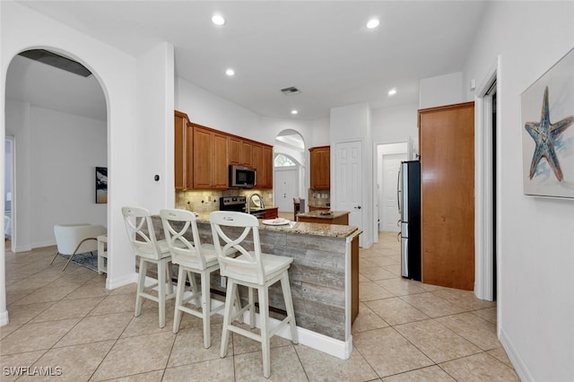 kitchen with a kitchen bar, light stone counters, light tile patterned floors, appliances with stainless steel finishes, and decorative backsplash