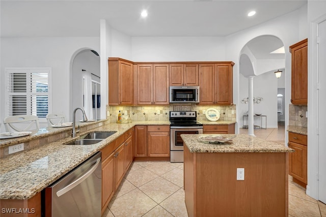 kitchen featuring light stone counters, appliances with stainless steel finishes, sink, and a kitchen island