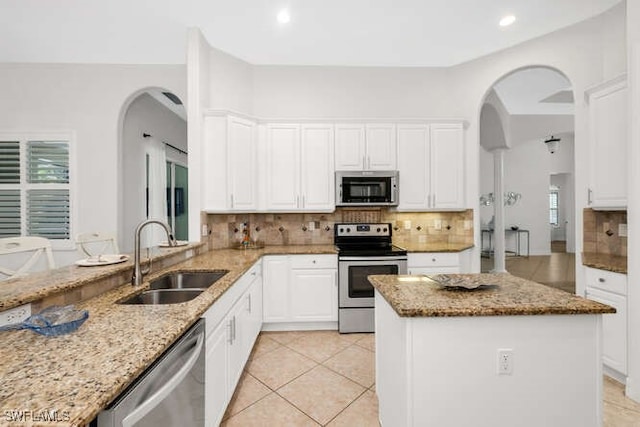 kitchen featuring light stone counters, a sink, arched walkways, stainless steel appliances, and white cabinetry