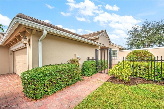 view of side of home featuring stucco siding, an attached garage, and fence