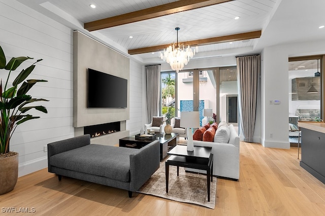 living room featuring a large fireplace, an inviting chandelier, beamed ceiling, and light wood-type flooring