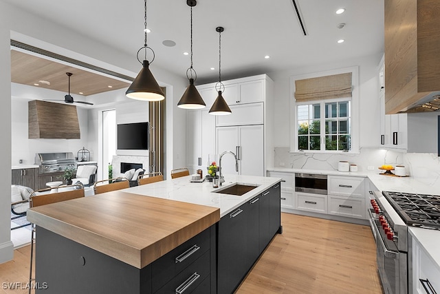 kitchen featuring a center island with sink, sink, white cabinetry, premium appliances, and pendant lighting