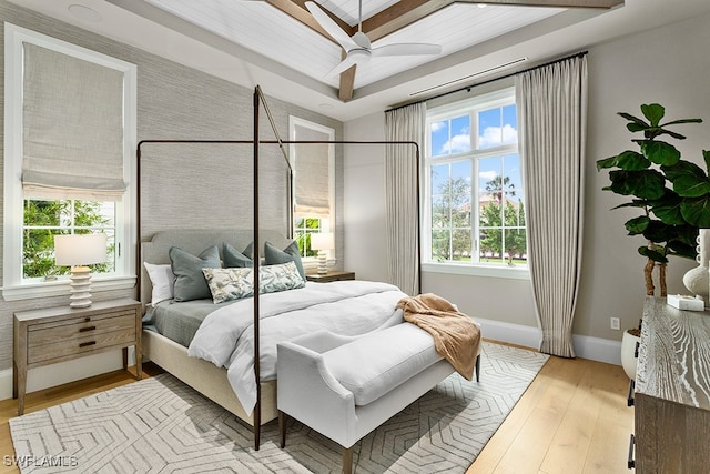 bedroom with light wood-type flooring, a tray ceiling, and ceiling fan