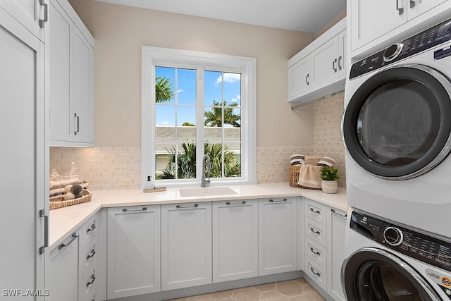 clothes washing area with stacked washer and dryer, cabinets, and sink