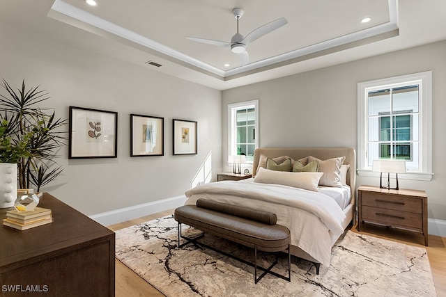 bedroom featuring multiple windows, a raised ceiling, and ceiling fan