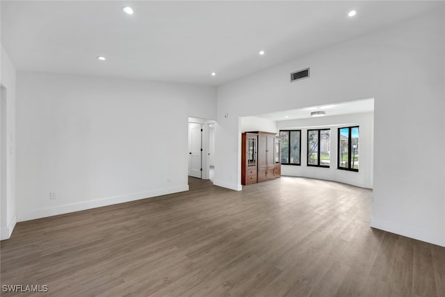 unfurnished living room featuring dark hardwood / wood-style flooring and a towering ceiling