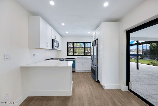 kitchen with light hardwood / wood-style floors, light stone counters, sink, white cabinetry, and appliances with stainless steel finishes