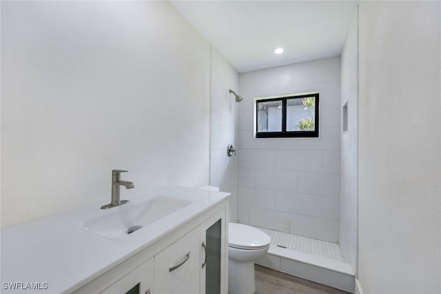 bathroom with hardwood / wood-style floors, vanity, toilet, and tiled shower