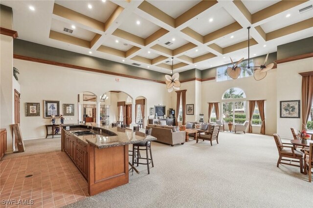 kitchen with light carpet, visible vents, coffered ceiling, arched walkways, and a sink