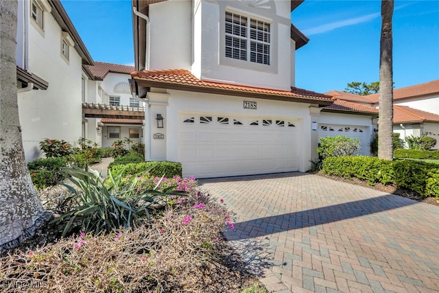 mediterranean / spanish-style home with a tiled roof, decorative driveway, an attached garage, and stucco siding