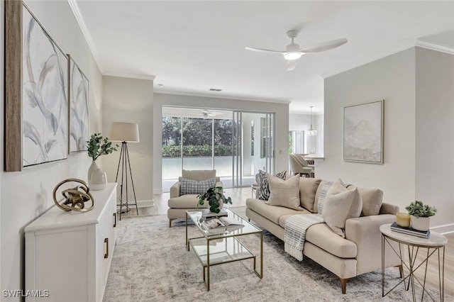 living area featuring baseboards, ornamental molding, light wood-style flooring, and a ceiling fan