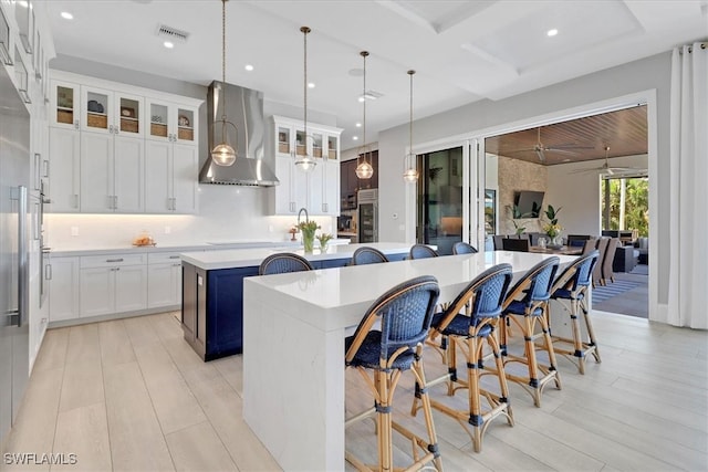 kitchen with pendant lighting, light hardwood / wood-style flooring, wall chimney exhaust hood, a kitchen island, and white cabinetry