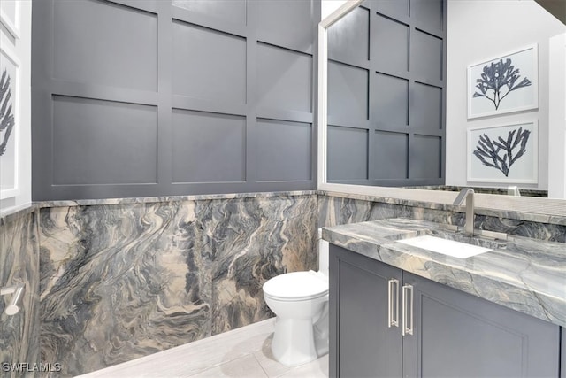 bathroom with tile patterned flooring, vanity, toilet, and tile walls