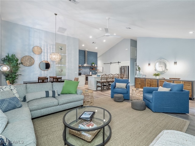 living room featuring ceiling fan with notable chandelier, wood-type flooring, a barn door, and high vaulted ceiling