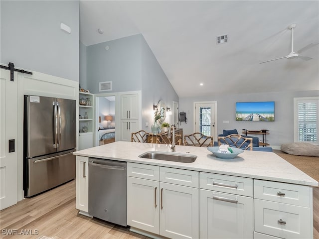 kitchen with white cabinets, sink, light hardwood / wood-style flooring, a barn door, and stainless steel appliances