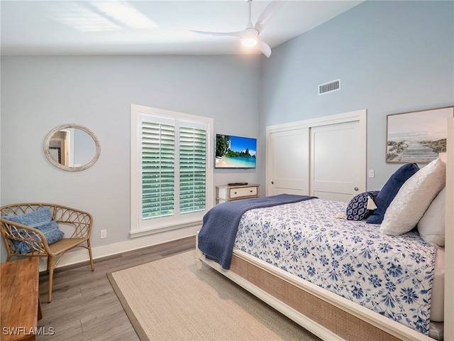 bedroom with hardwood / wood-style flooring, ceiling fan, high vaulted ceiling, and a closet