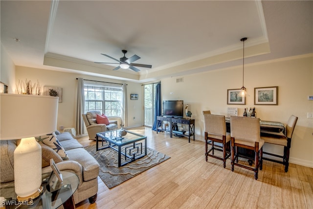 living room with a tray ceiling, light hardwood / wood-style flooring, ceiling fan, and crown molding