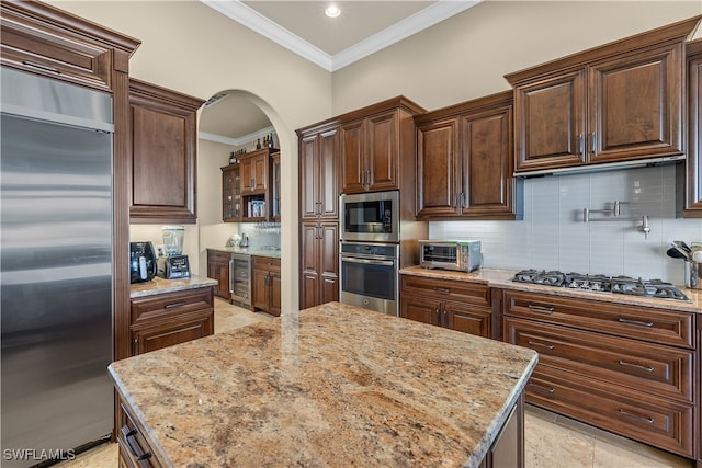 kitchen featuring tasteful backsplash, built in appliances, light stone countertops, and beverage cooler