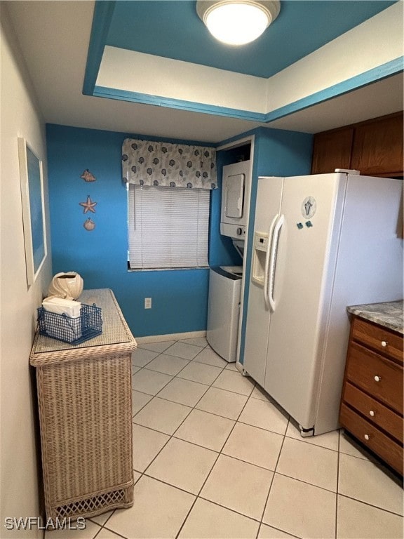 kitchen with stacked washing maching and dryer, white fridge with ice dispenser, and light tile patterned flooring