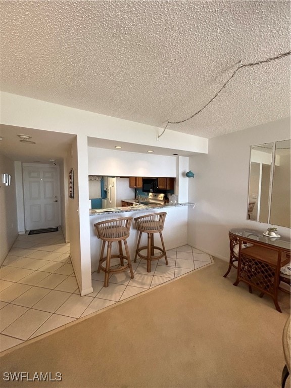 kitchen with kitchen peninsula, a textured ceiling, light colored carpet, and a breakfast bar