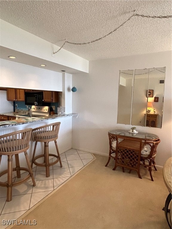 kitchen featuring a textured ceiling, light carpet, a breakfast bar, and kitchen peninsula