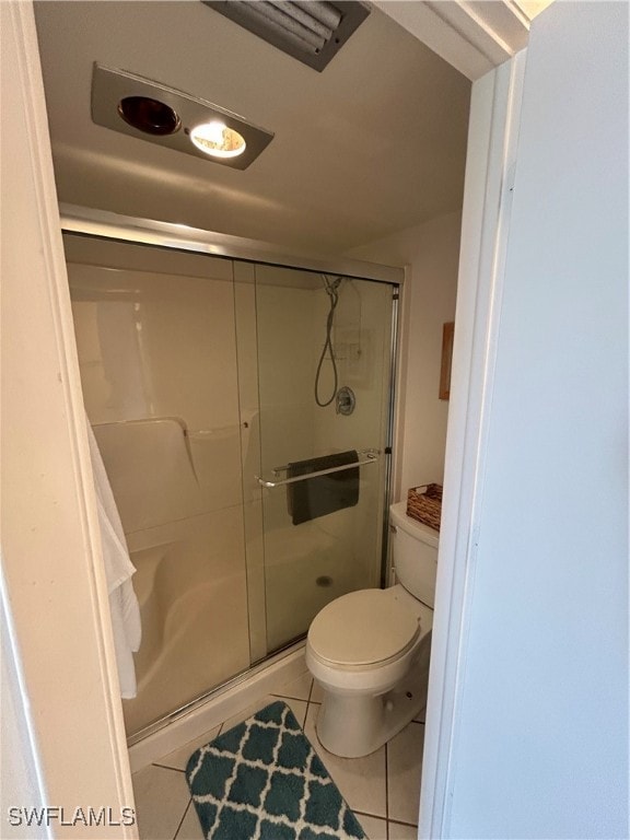 bathroom featuring tile patterned flooring, toilet, and a shower with door