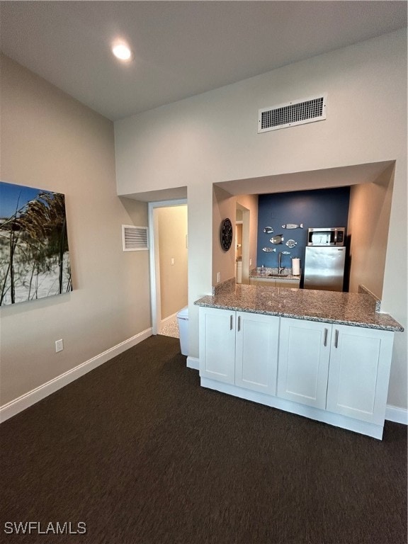 kitchen with dark stone counters, white cabinetry, dark carpet, and stainless steel fridge