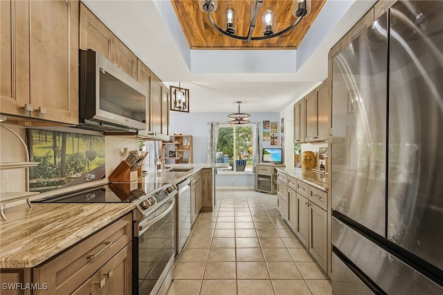 kitchen with stainless steel appliances, light tile patterned floors, a raised ceiling, pendant lighting, and an inviting chandelier