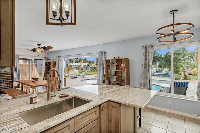 kitchen with sink, a kitchen breakfast bar, ceiling fan with notable chandelier, light tile patterned floors, and decorative light fixtures