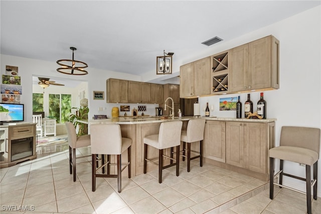 kitchen with light brown cabinets, kitchen peninsula, ceiling fan with notable chandelier, and light tile patterned flooring