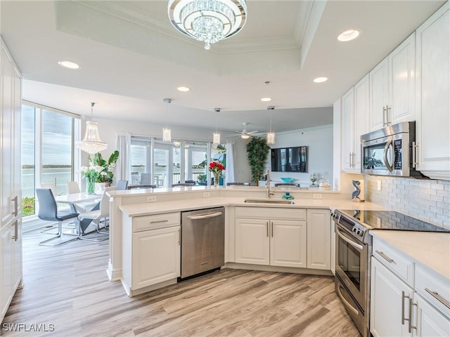 kitchen featuring white cabinets, sink, a tray ceiling, kitchen peninsula, and stainless steel appliances