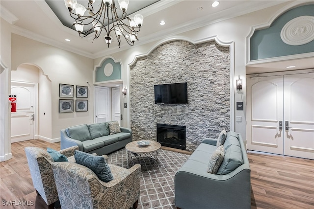 living room with a stone fireplace, hardwood / wood-style floors, a towering ceiling, and ornamental molding