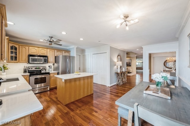 kitchen with a center island, ceiling fan with notable chandelier, dark hardwood / wood-style floors, ornamental molding, and appliances with stainless steel finishes