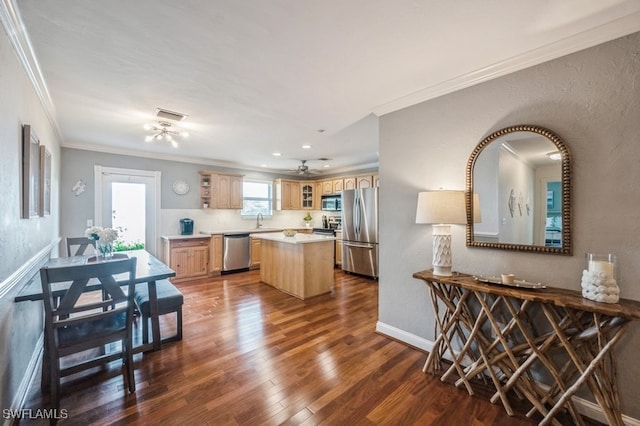 kitchen with sink, dark wood-type flooring, crown molding, a kitchen island, and appliances with stainless steel finishes