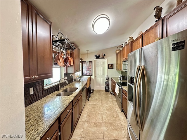 kitchen featuring light stone counters, stainless steel appliances, decorative light fixtures, sink, and vaulted ceiling