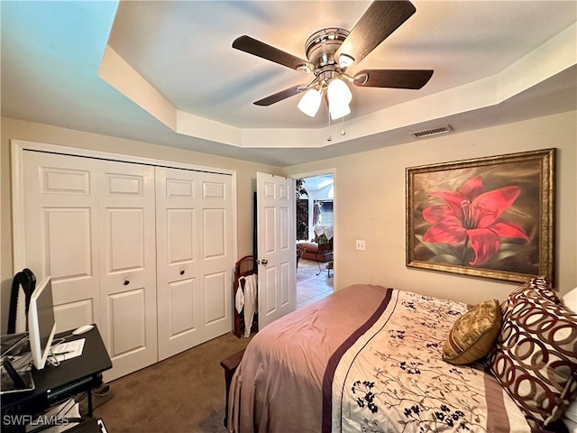 bedroom with ceiling fan, dark colored carpet, a closet, and a tray ceiling