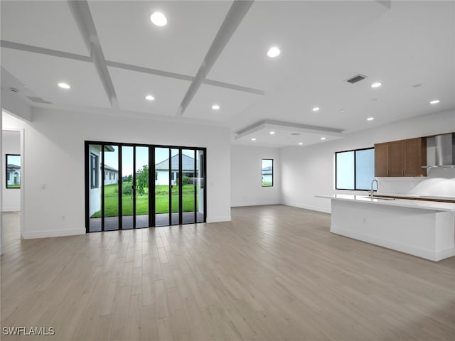 unfurnished living room featuring light wood-type flooring, coffered ceiling, sink, and a healthy amount of sunlight