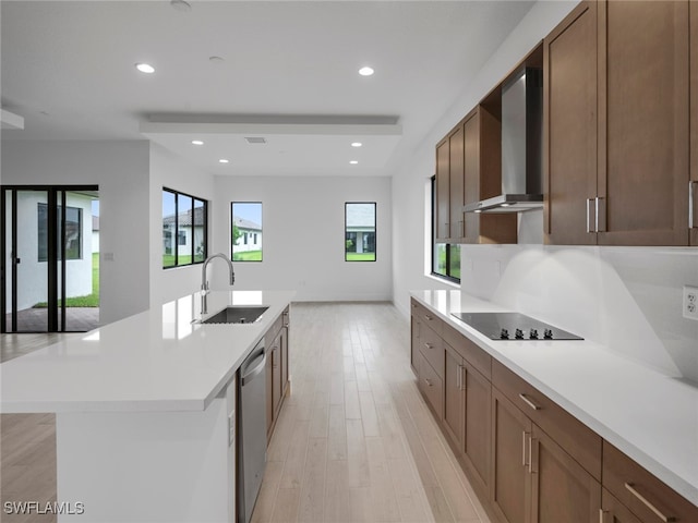 kitchen featuring black electric stovetop, light wood-type flooring, sink, wall chimney exhaust hood, and a kitchen island with sink