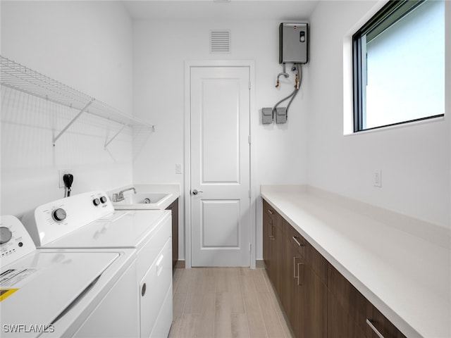 laundry room featuring cabinets, water heater, sink, washer and clothes dryer, and light hardwood / wood-style flooring