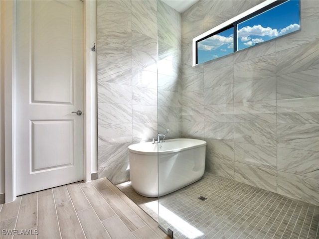 bathroom with tile walls, hardwood / wood-style floors, and a bathtub