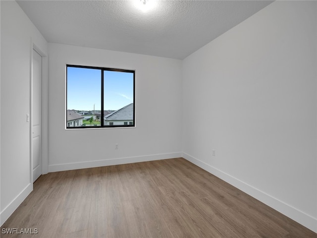 empty room with light wood-type flooring and a textured ceiling