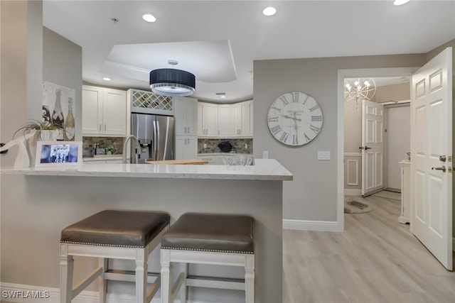 kitchen featuring kitchen peninsula, stainless steel refrigerator with ice dispenser, decorative backsplash, light stone counters, and white cabinetry