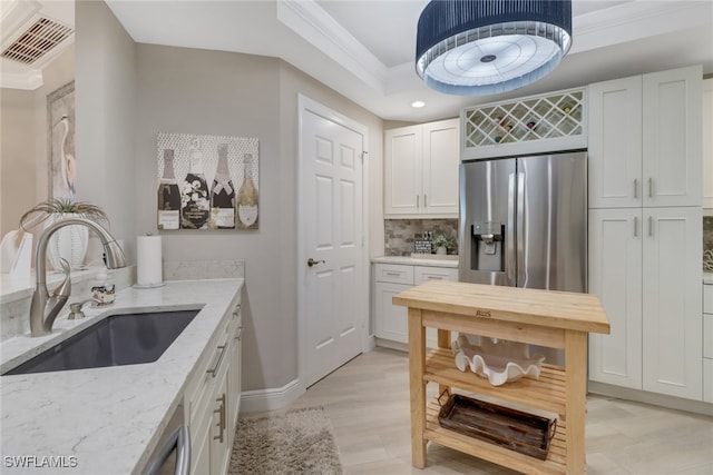 kitchen with light stone countertops, stainless steel fridge, white cabinetry, and sink