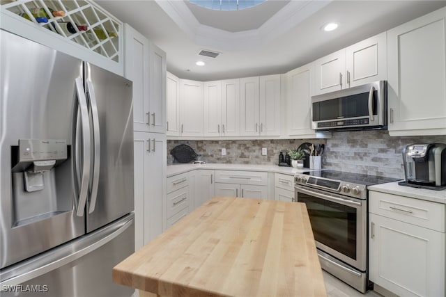 kitchen with backsplash, ornamental molding, stainless steel appliances, a raised ceiling, and white cabinets