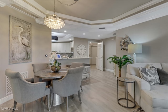 dining area with a tray ceiling, light hardwood / wood-style flooring, a notable chandelier, and ornamental molding