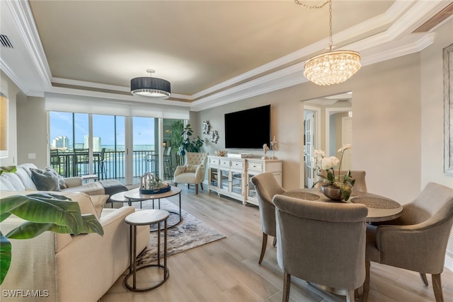 living room with a tray ceiling, crown molding, a chandelier, and light wood-type flooring